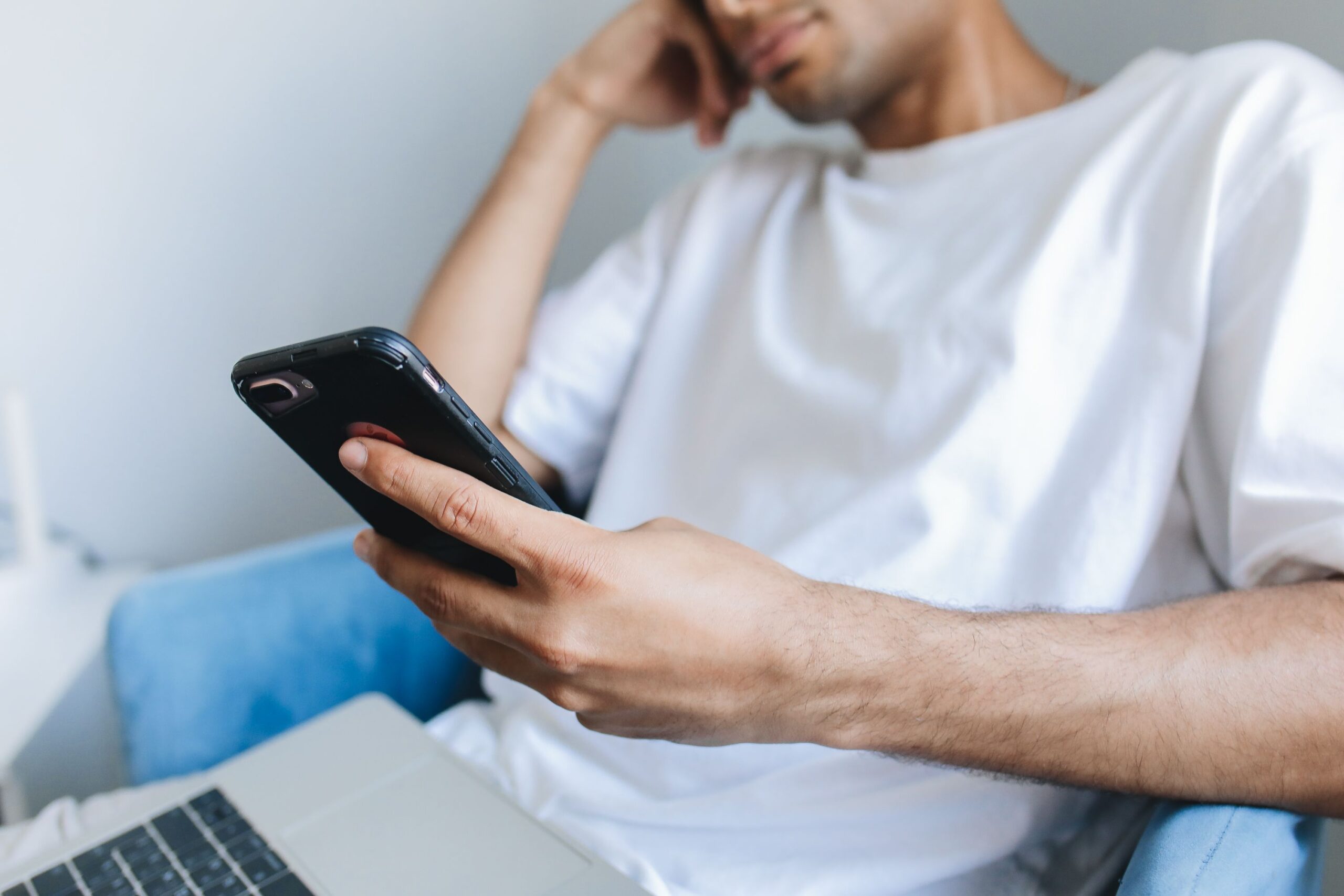ソファでスマートフォンを手にし、こめかみに手をあてる人物