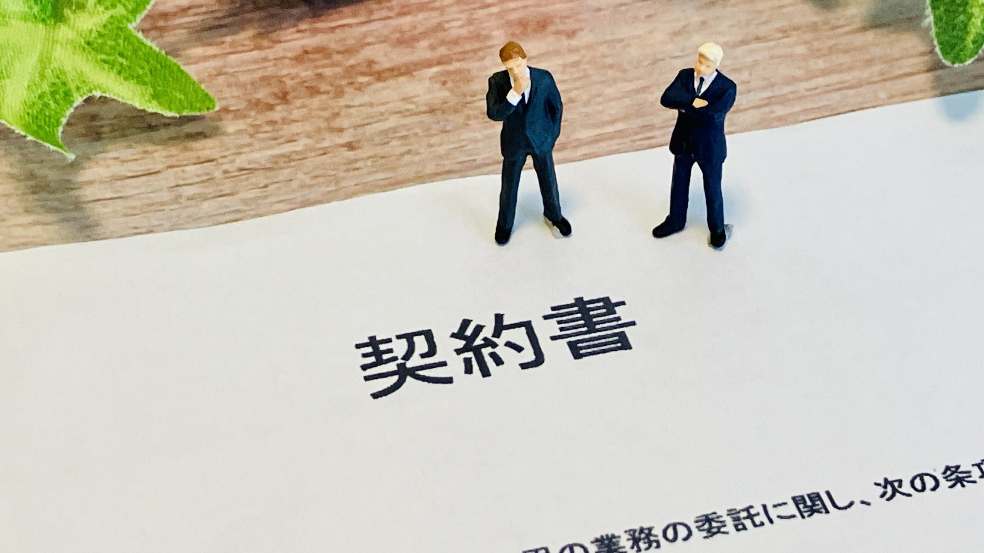 テーブルに広げた契約書の上に立つ、スーツ姿のミニチュア人形